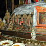 Offering bowls, butter lamps, and silk scarves offered to various small statues of Buddhas and lamas.