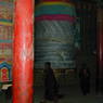 Tibetan women spinning a large prayer wheel wrapped in prayer flags.