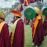 A procession of monks wearing yellow hats and playing clarinets (gyaling) and pole drums.