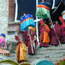 A procession of monks wearing red hats and carrying parasols.