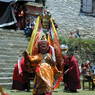A smaller masked dancer (foreground) and a dancer dressed as Padmasambhava (background) in the courtyard.