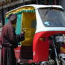 An elderly beggar woman talking to a motor rickshaw driver.